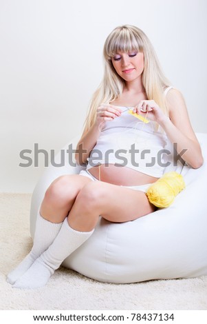 A blond pregnant woman knitting for her unborn baby