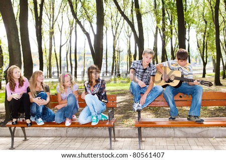 Teenage guy playing guitar, his friends listening