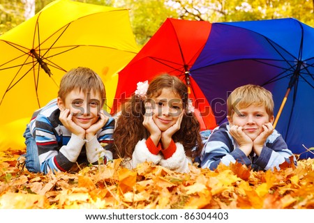 Three children lying under three colorful umbrellas