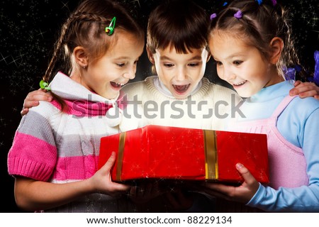 Three excited kids look happily into Christmas gift - stock photo
