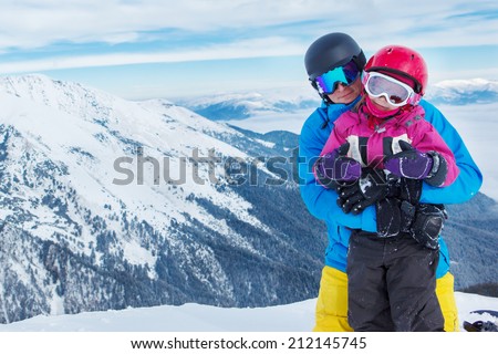 Father and daughter with ski helmets on, in winter mountains