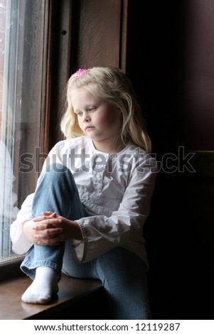 Pretty, blonde girl sitting on a window sill with her knee up.