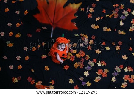 Pretty little girl dressed in a pumpkin costume, watching leaves fall from above; shot from above.
