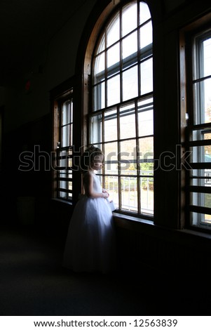 Little bridesmaid looking out a large, wood-paned window.