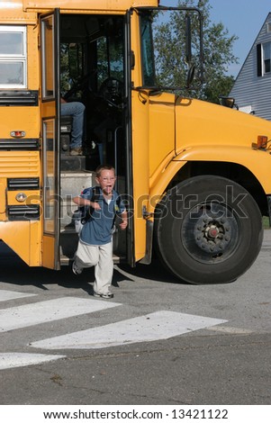 Happy boy with glasses getting off the yellow school bus after the first day of school.