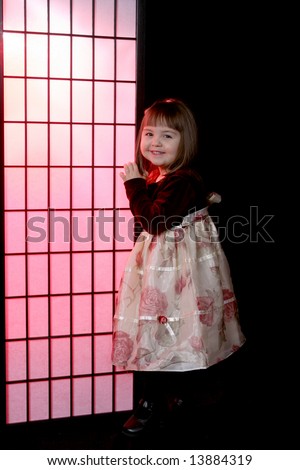 Pretty little girl in flowered party dress and standing next to a pink screen.