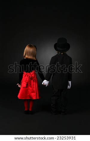 boy and girl in formal clothing standing back to and holding hands