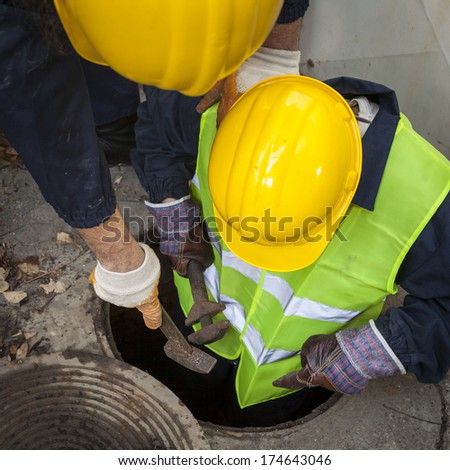 Two young manhole workers, one of them being in the sewer looking for problem to fix.