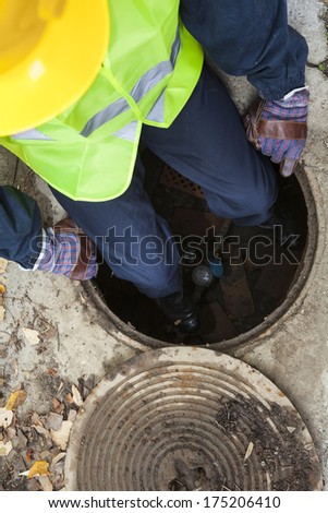 Manual worker inside of manhole fixing water pipeline, holding hammer. View from directly above.
