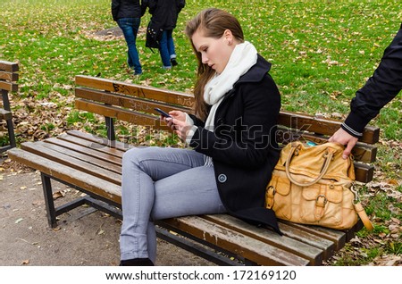 Pickpocket stealing handbag while woman using mobile phone on bench in park