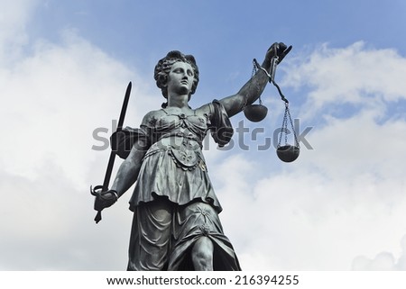 Statue of Justice with sword and scales in front of a blue cloudy sky