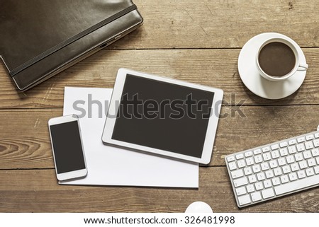 blank phone and tablet device placed over empty white paper sheets on a wooden workspace