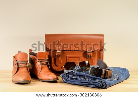 Still life with Brown leather shoes, leather bag, jeans and sunglasses on wooden table