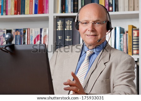 Friendly smiling man with headphones, notebook and webcam, telephoning via skype, copy space