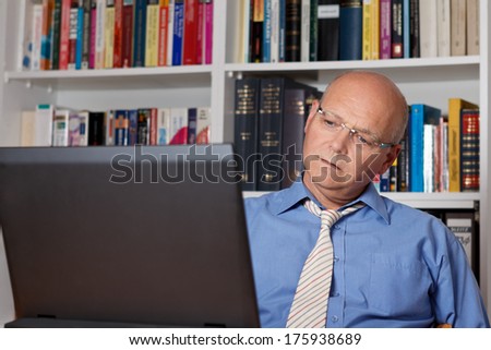 Thoughtful man staring at his laptop in front of bookshelves, copy space