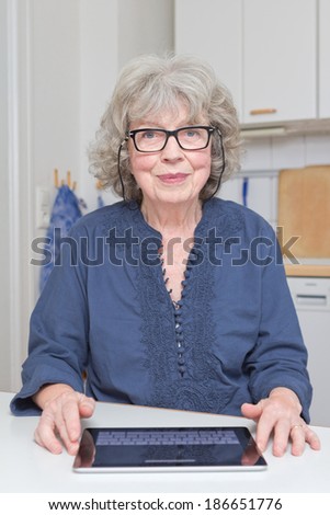 Happy old woman with tablet-pc in her kitchen