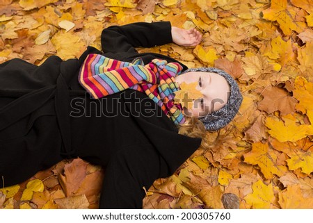 Young woman lying on yellow maple leaves and peering cross-eyed at a leaf on her nose, copy space