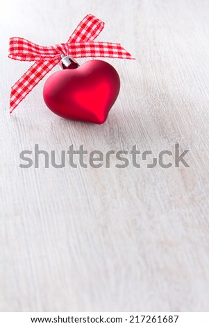 Xmas decoration in shape of a heart with a bow of red and white checkered ribbon, wooden background, copy space
