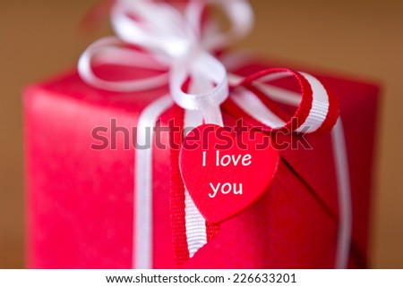 Red present with white bow and heart on brown background, text, I love you