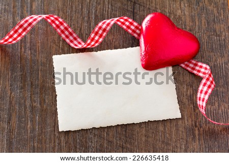 Old card on dark wood with big red heart an red and white checkered ribbon in loops, country setting, copy space