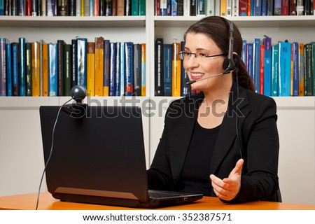 Teacher, tutor or professor with headset, laptop and camera in her office explaining something at an online lesson or video lecture, webinar