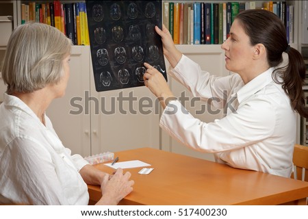 2 women in a  surgery: middle aged doctor in lab coat showing her senior patient magnetic resonance images of her head