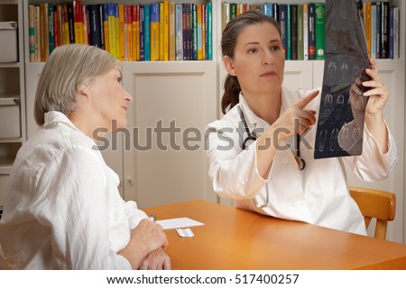 Experienced doctor in white coat showing her female patient on an image of ct-scans of her brain where the tumor is located