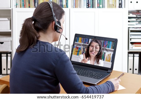 Woman with pen and paper and a headset in front of her laptop making a video call with her friendly tutor, text space