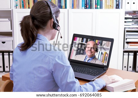 Woman with a headset in front of her laptop and a book making an online video call with her friendly teacher, text space, e-learning concept