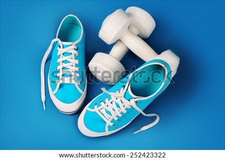 Turquoise gym shoes and white dumbbells on a blue sports mat.