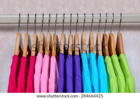 Pink, purple, crimson, bright green and turquoise women\'s T-shirts hanging on wooden hangers on light background. Side view.