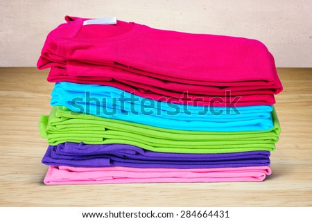 Pink, purple, crimson, bright green and turquoise women\'s T-shirts lie pile on a wooden and pink background.