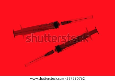 Two plastic disposable syringes with a needles in the protective caps on red background
