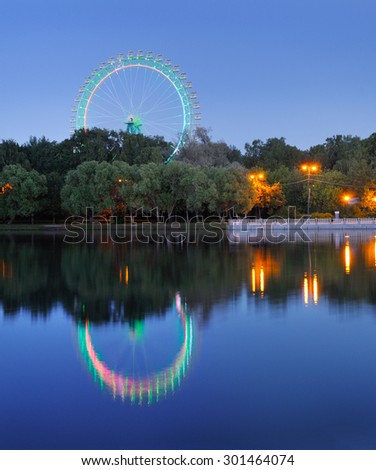 Ferris wheel in the park with colorful illumination against the night blue sky and reflection in the pond
