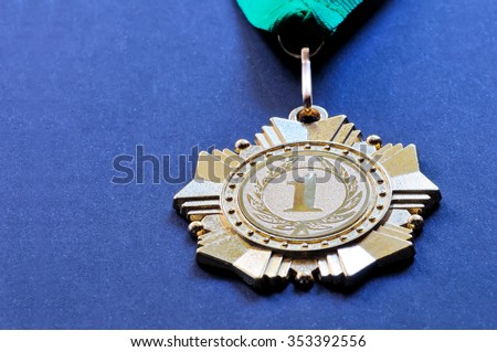 Metal medal of gold color for the winner for the first place with a ribbon of green color on a blue background