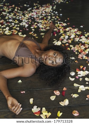 Beautiful young woman surrounded with rose petals lying on her back on a wooden floor in a bikini looking up at the camera with a serious expression