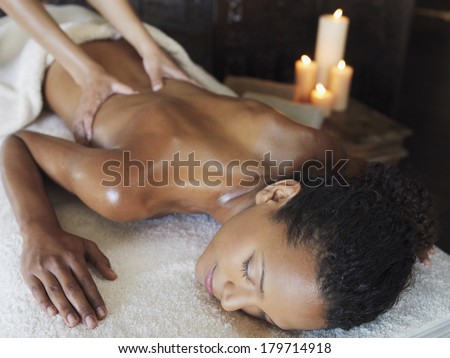 Young Asian woman enjoying a spa and beauty treatment and massage as she lies on her stomach with the masseuse manipulating her back muscles with a background of burning candles