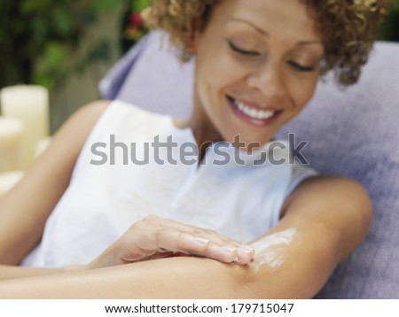 Beautiful happy woman relaxing in the garden smiling as she applies sunscreen or skin cream in a skincare and beauty concept