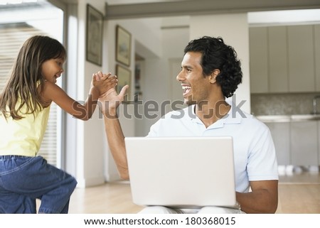 Father using laptop computer at home with his daughter giving him a hi-five