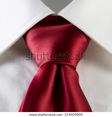 Close up of a businessman wearing a red necktie with the collar of a plain white shirt and knot of the tie in frame