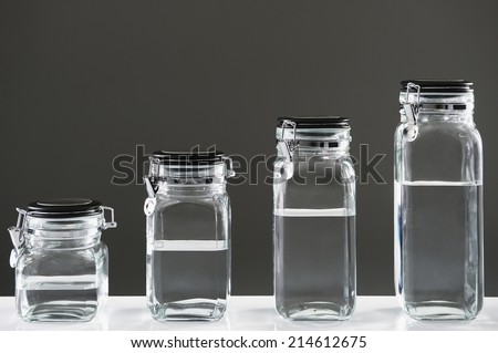 Different sized jars lined up from smallest to biggest with water on gray background