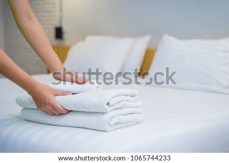 Close-up of hands putting stack of fresh white bath towels on the bed sheet. Room service maid cleaning hotel room.