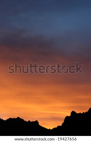 An intense orange and blue cloudy sunset, with black mountains on the base