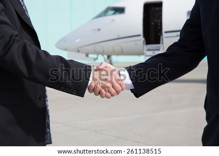 Businessmen shake hands in front of a corporate jet