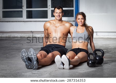 Man and woman - fitness team sitting on floor with kettlebells