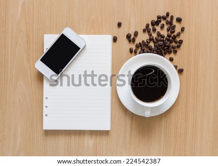 Smart phone with blank screen area on white notebook paper sheet and coffee cup on wooden background.