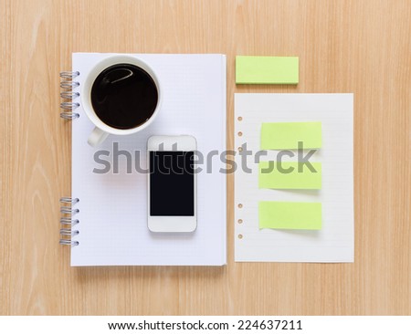 Coffee cup, smart phone, notebook, paper stick and white paper on wooden background.