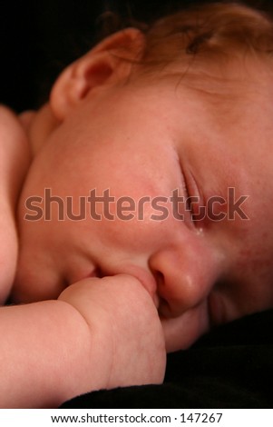 Photo of a baby sleeping with her hand close to her face.