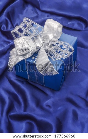 Christmas gift box on blue satin background, with silver ribbon.