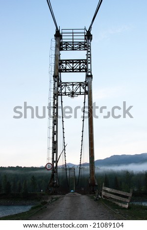 Old suspension (guyed) bridge over Katun\' river in morning fog, Altai